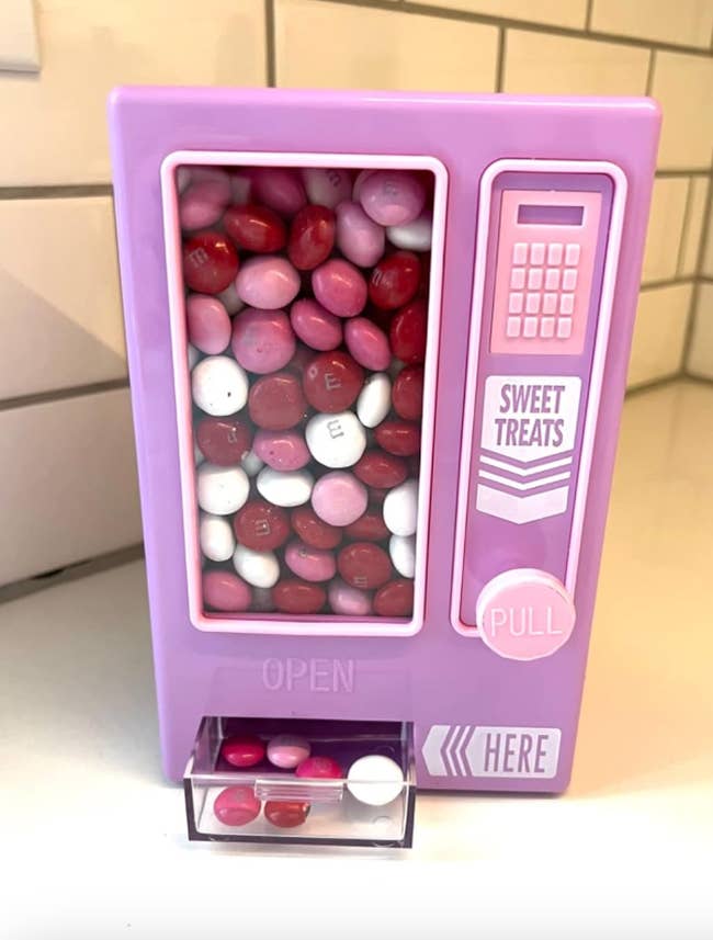 Miniature pink candy dispenser with assorted pink and red candies visible inside