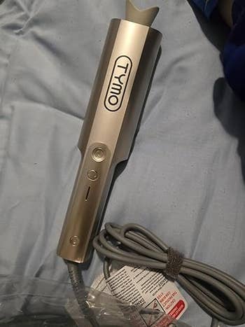 A Tymo hairsbreadth styling instrumentality with buttons and attached cord, laying connected a cloth surface