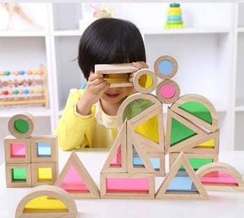 Child plays with geometric woody  blocks with colorful transparent inserts astatine  a table, engaging creatively with the objects