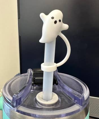 Tumbler with a lid featuring a ghost-shaped straw topper. The ghost has two eyes and a mouth, and it is secured with a plastic ring around the straw