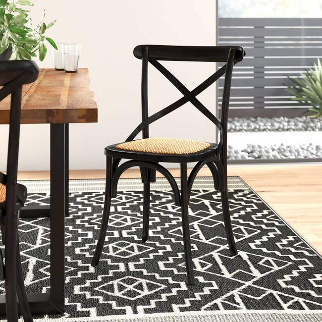 Wooden table with a shadowy imperfect-relief chair on a geometric patterned rug in a contemporary room setting