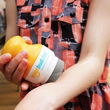 model using the solar buddy to apply sunscreen on their arm