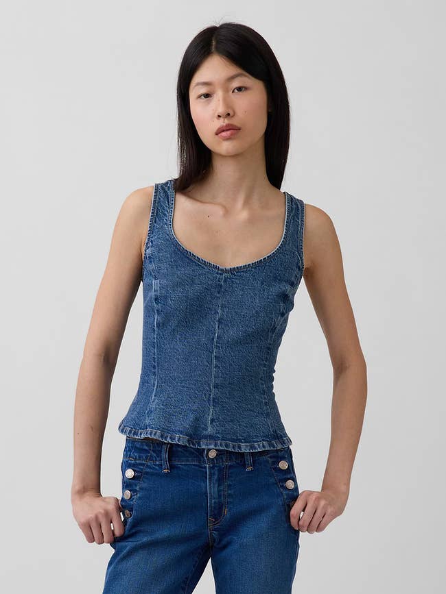 Person wearing a denim vessel  apical  and jeans with fastener  details, posing against a plain background