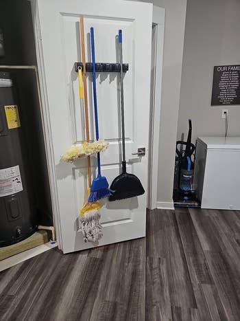reviewer image of brooms and mops hanging from the organizer which is mounted to the inside of a closet door