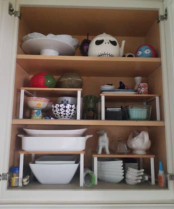 another reviewer's four white and natural shelves in a cabinet holding bowls, plates, cups, and other items