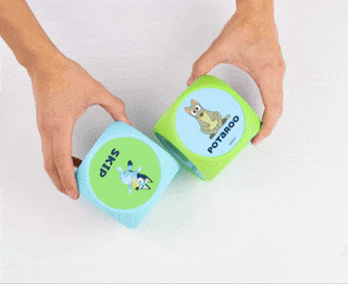Hands holding and rolling two soft dice with animal images and text on their sides, used for a shopping article