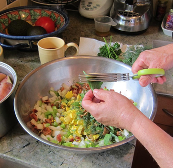 reviewer using the scissors to cut up herbs over a salad bowl