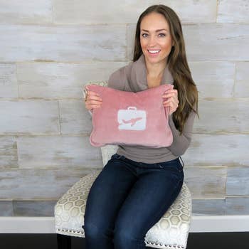a model holding a pink pillow and blanket set stored in a fluffy pink travel pouch