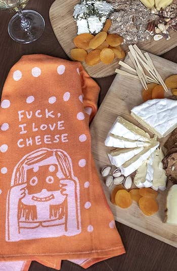 dish towel with illustrated face holding up a slice of cheese. text says fuck, i love cheese.