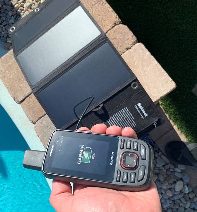 reviewer holding a handheld gps that's connected to a solar charger laid out by a pool