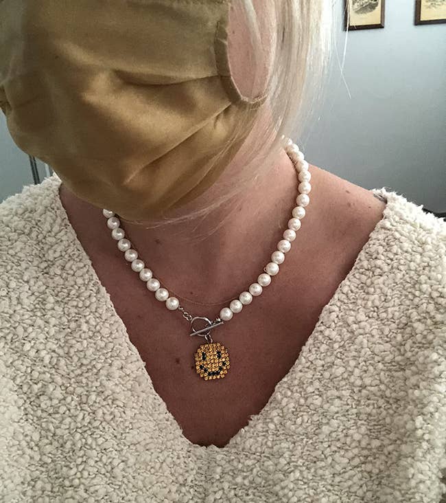reviewer wearing the pearl necklace with smiley face charm in the middle
