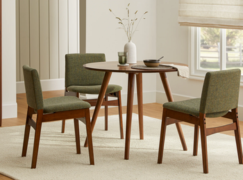 Four mid-century modern dining chairs around a small round table in a neutral-toned room