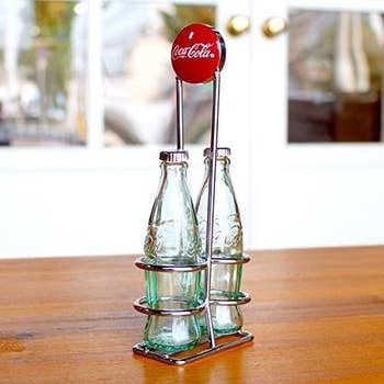 Two small coke bottle shaped shakes in a silver holder with a coca cola logo on it 