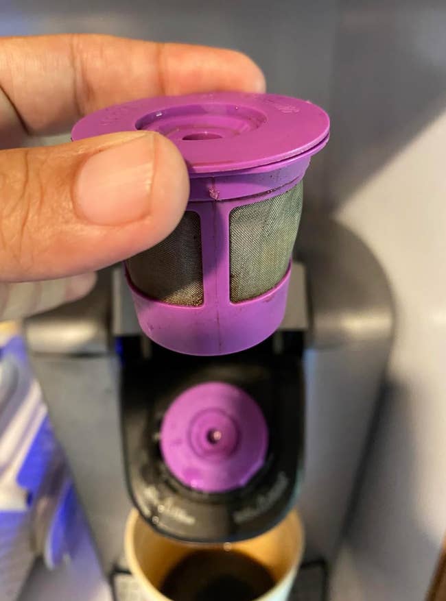 Person holds a reusable coffee filter pod above a coffee machine