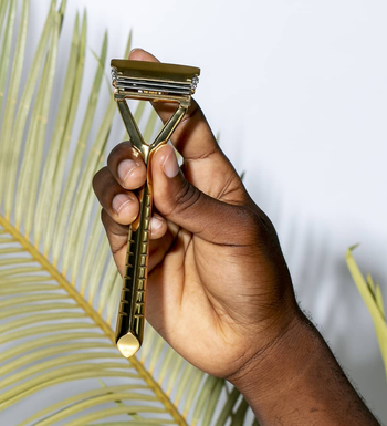 a hand holding the metal leaf razor in gold 