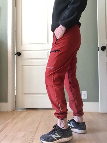 side profile of reviewer showing zippered pockets and adjustable ankle area on red version of pants
