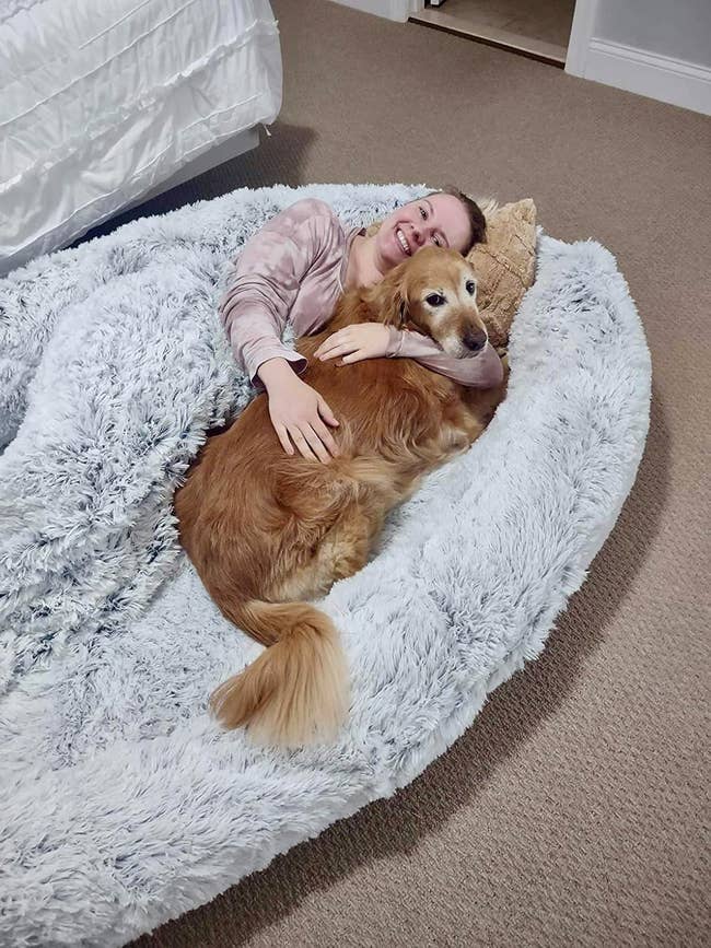 Person relaxing with a large dog in a cozy, fluffy bed, conveying comfort and warmth