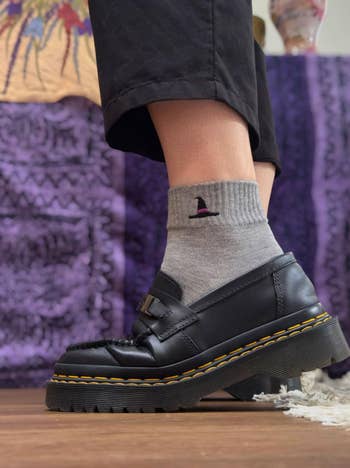 Person wearing achromatic loafers and grey socks with a tiny chapeau design, lasting connected a wood level with a patterned backdrop