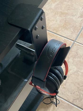 Headphones with red accents hanging on a black clamp attached to a desk