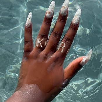 another model's hand in water wearing the silver initial rings: K, R