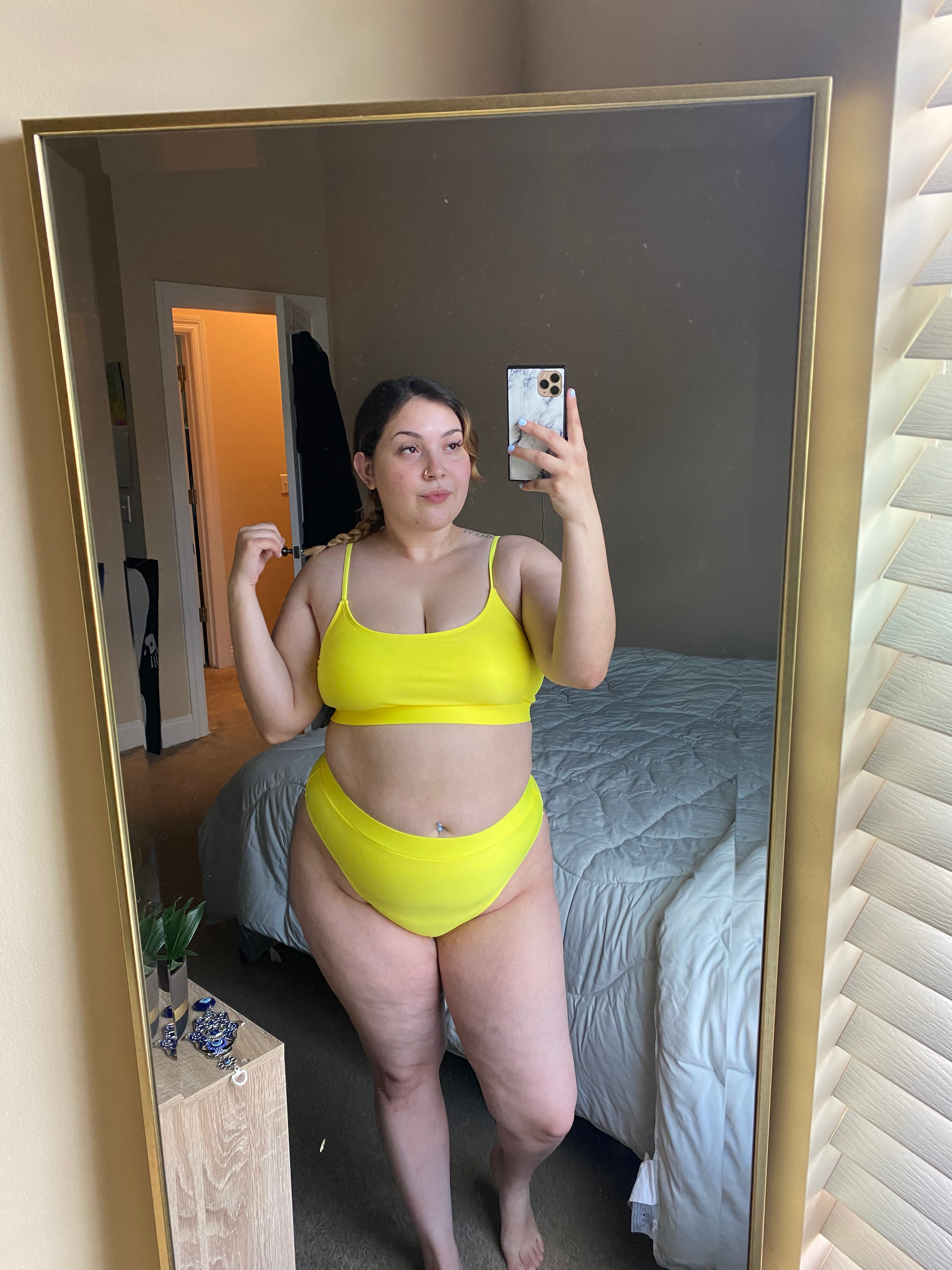 Person taking a mirror selfie wearing a stylish two-piece swimsuit in a bedroom, showcasing swimwear for a fashionable shopping article
