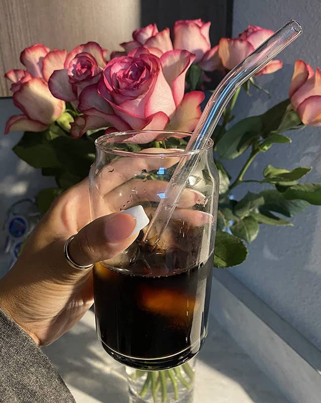 Reviewer holding clear can-shaped glass with an open top full of iced coffee 