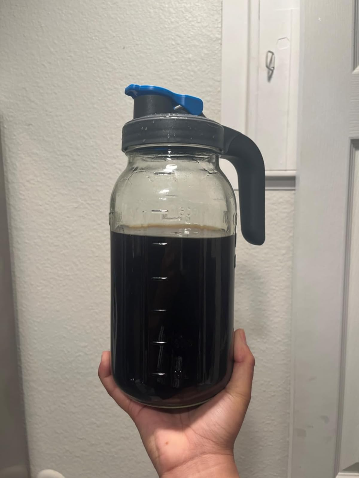 Hand holding a ample  solid  jar filled with acheronian  liquid, featuring a grip  and spout