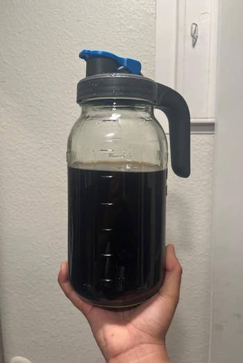 Hand holding a ample solid jar filled with acheronian liquid, featuring a grip and spout