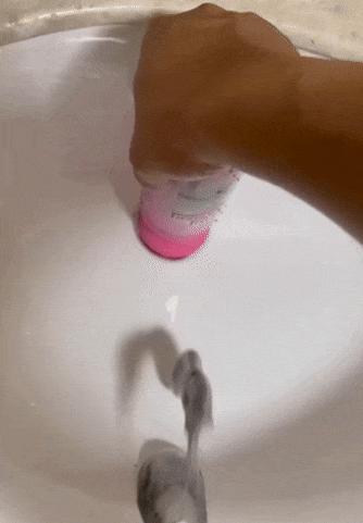 Liquid soap being dispensed into a descend  from a pinkish  bottle