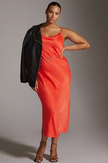 model wearing the red dress with heels and a belt, with a leather jacket slung over their shoulder