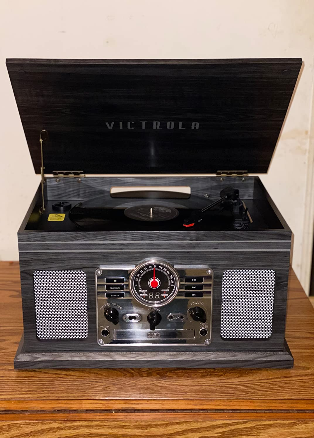 Reviewer image of gray and black vintage-inspired wooden turntable with custom buttons and three dials on the front and black vinyl and needle on it, sitting atop brown wooden table