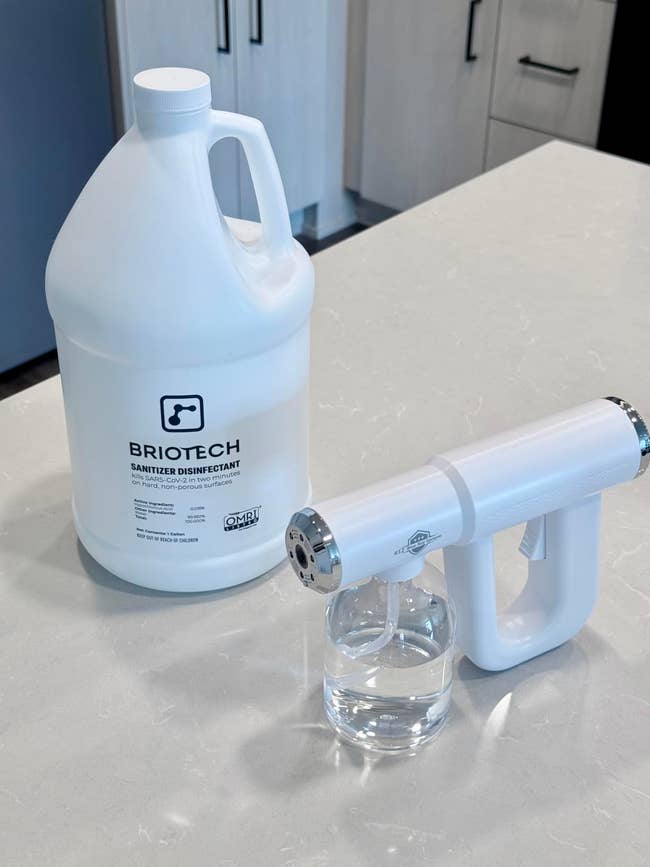 Counter with a large jug of Briotech sanitizer and a spray device, positioned for cleaning or disinfecting purposes