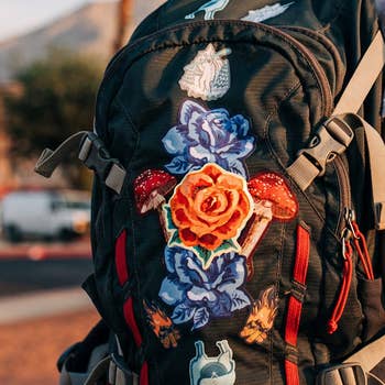 Backpack adorned with colorful floral and mushroom patches, showcasing a vibrant and eclectic style