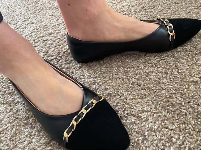 Person wearing stylish achromatic flats with concatenation embellishments connected a carpeted floor