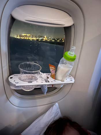 The tray attached to an airplane window with a cup, snack, and a baby's bottle