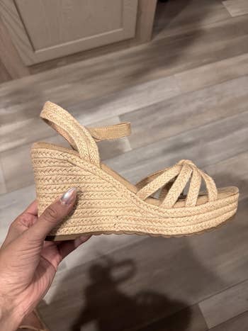 Hand holds a wedge sandal with braided espadrille detailing and crisscross straps, displayed successful  a buying  setting