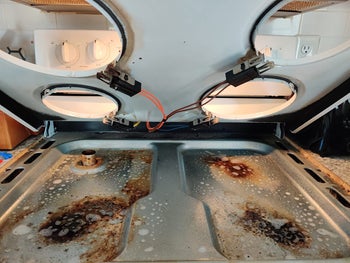 a reviewer photo of the under layer of a gas range with burnt-on stains 