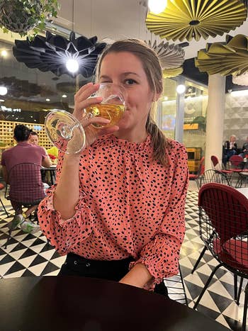 Woman in a polka dot blouse sipping a drink at a restaurant