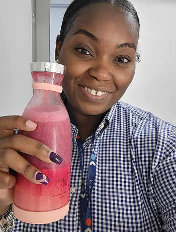 Reviewer holding small milk jar shaped pink blender with smoothie in it