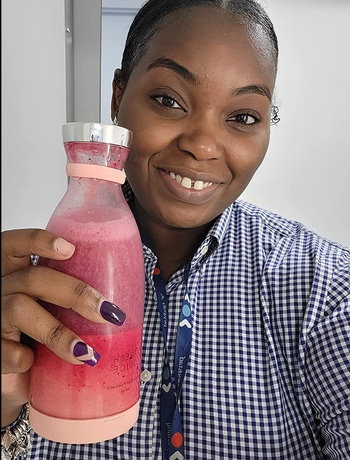 Reviewer holding small milk jar shaped pink blender with smoothie in it 