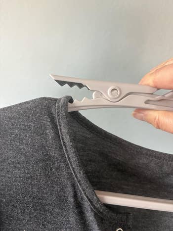 Close-up of a manus  utilizing a integrative  clip to unafraid  a acheronian  garment  connected  a hanger, demonstrating covering  care