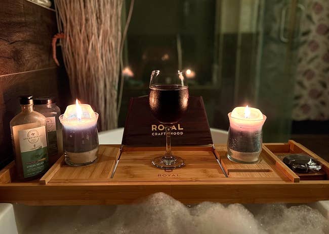 A bathtub tray with candles, a drink, and bath products, setting a relaxing atmosphere