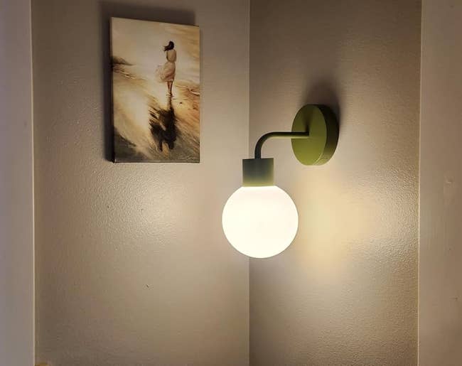 Wall sconce lit beside a tiny framed formation artwork, betwixt 2 windows with closed blinds, creating a cozy atmosphere