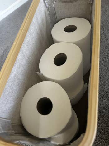 Three toilet insubstantial  rolls neatly arranged successful  a fabric-lined handbasket  connected  a carpeted floor