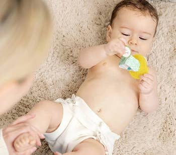 Baby successful a diaper plays with a artifact connected a brushed rug, with an big mildly holding their leg. Large substance reads