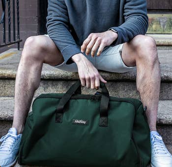 a model sitting on a stoop with a green duffel bag 