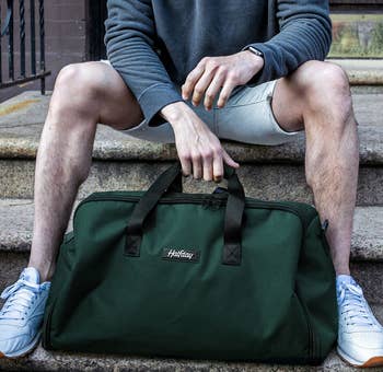 a model sitting on a stoop with a green duffel bag 