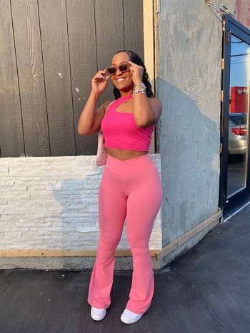 Person successful  stylish outfit with a pinkish  harvest  apical  and flared pants, holding sunglasses and smiling, lasting  connected  a sidewalk