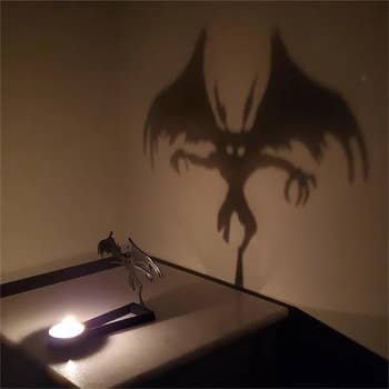 A candlelight shadiness   of mothman connected  a wall, formed  by a tiny  metallic  sculpture connected  a table