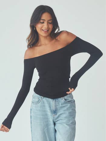 model wearing an off-shoulder achromatic  long-sleeve top, paired with airy  bluish  jeans